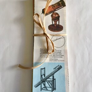May include: A vintage book with a brown ribbon tied around it. The book features a black and white illustration of a telescope on a stand. The book includes a quote from William Blake: "Now I a fourfold vision see, And a fourfold vision given to me. Tis fourfold in my  eme delight, And three fold Beulahs night, And twofold Iways. May God us keep, From Single vision & Newtons sleep (from a letter to a friend)"
