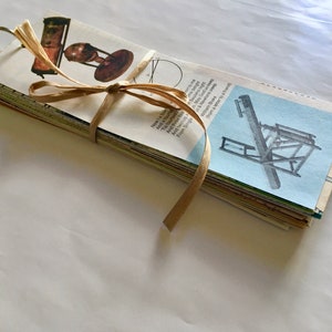May include: A stack of vintage paper cards tied with a brown ribbon. The cards feature illustrations of scientific instruments, including a telescope, a globe, and a printing press. The cards are bound together with a metal ring.