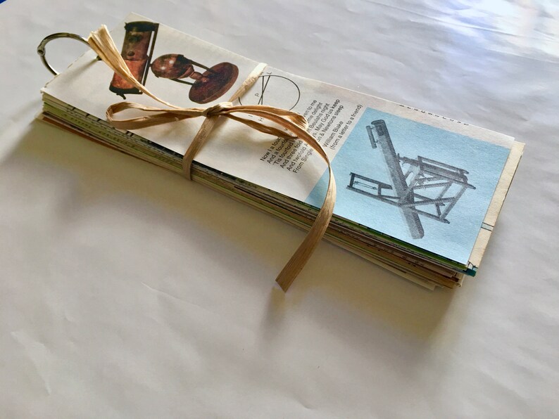 May include: A stack of vintage paper cards tied with a brown ribbon. The cards feature illustrations of scientific instruments, including a telescope, a globe, and a printing press. The cards are bound together with a metal ring.
