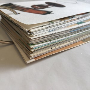 May include: A stack of vintage postcards bound together with a silver ring. The postcards are various colors and feature different images.