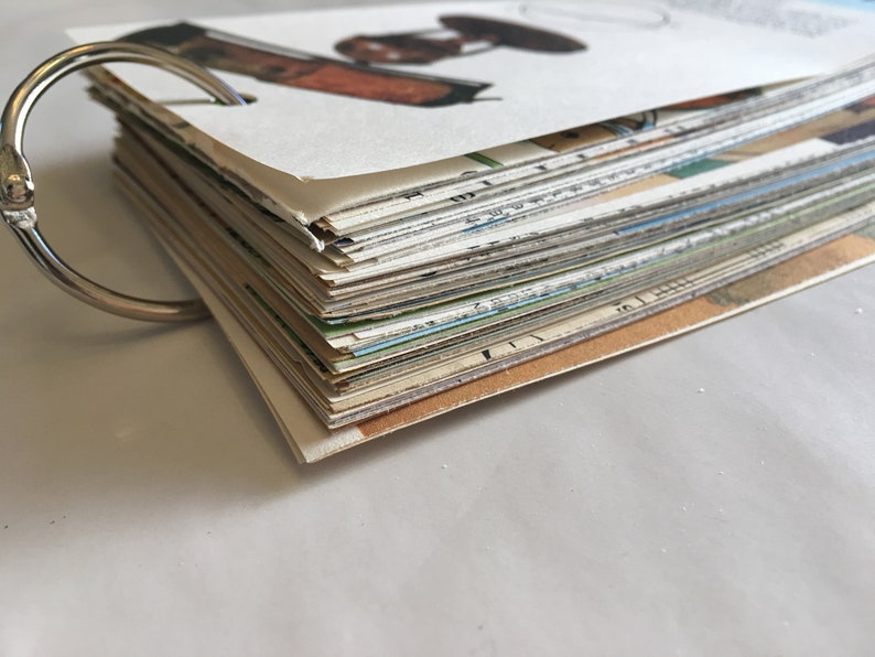 May include: A stack of vintage postcards bound together with a silver ring. The postcards are various colors and feature different images.