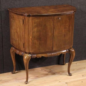 May include: A vintage wooden cabinet with a curved front and two doors. The cabinet is supported by four curved legs and features a decorative carved apron. The wood has a warm, brown tone.