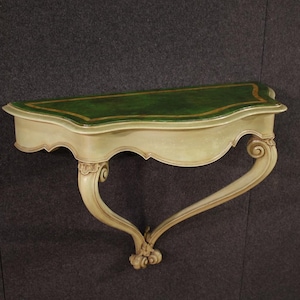May include: A wall-mounted console table with a green top and cream-colored base. The table features a curved design with ornate, scroll-like legs and a gold trim around the top. The table is a decorative piece of furniture.