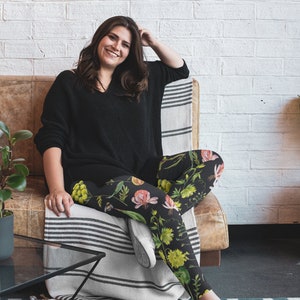 May include: A woman wearing black leggings with a floral print featuring yellow, pink, and green flowers. She is sitting on a brown leather couch with a white and black striped throw blanket.