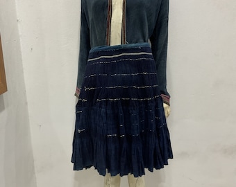 May include: A blue and teal traditional skirt with pleats and a matching jacket. The skirt has a white and gold trim.