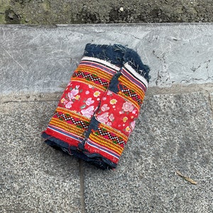 May include: A folded piece of fabric with a red background and floral pattern. The fabric has a black and white trim with yellow and orange accents.