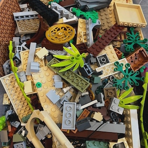 May include: A large pile of colorful Lego bricks, including green, brown, and tan pieces. The bricks are arranged in a random pattern, and some of them are stacked on top of each other. There are also some small green plants and a few larger pieces, such as a brown door and a tan window.