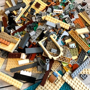 May include: A collection of various-sized tan, brown, gray, black, and teal building blocks. The blocks are scattered, with some appearing to be part of a larger structure. There are also some specialized pieces, such as a light tan frame.