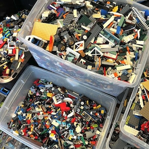 May include: Two clear plastic storage containers filled with a large assortment of colorful Lego bricks. The bricks are a mix of different sizes, shapes, and colors, including red, blue, green, yellow, and black.