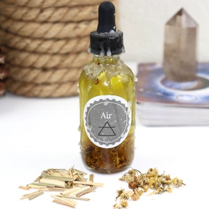 May include: A clear glass bottle with a black dropper top and a white label that says "Air" with a triangle symbol. The bottle is filled with a yellow liquid and there are dried flowers and herbs at the bottom.