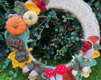 May include: A crocheted autumn wreath with a burlap base. The wreath is decorated with crocheted pumpkins, leaves, acorns, and mushrooms in shades of orange, brown, green, and red.