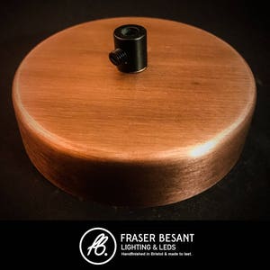 May include: A copper ceiling rose with a black metal threaded fitting. The rose is smooth and has a brushed finish.