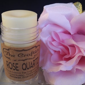 May include: A small, clear plastic container with a white solid lotion bar inside. The container has a brown label with the text "The Craftst ROSE QUARTZ Solid Lotion Bar Ingredients Cocoa butter, Coconut oil Beeswax, Essential oils".