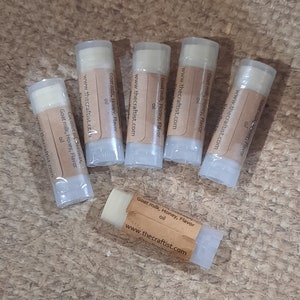 Op de afbeelding: Zes kleine buisjes lippenbalsem met bruine etiketten. De etiketten hebben de tekst "Goat milk, Honey, Flavor oil" en "www.thecraftist.com".