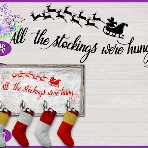 May include: A white wooden sign with the text "All the stockings were hung..." in red lettering. There are four red and white stockings hanging on hooks below the sign. The sign is on a white wood background.