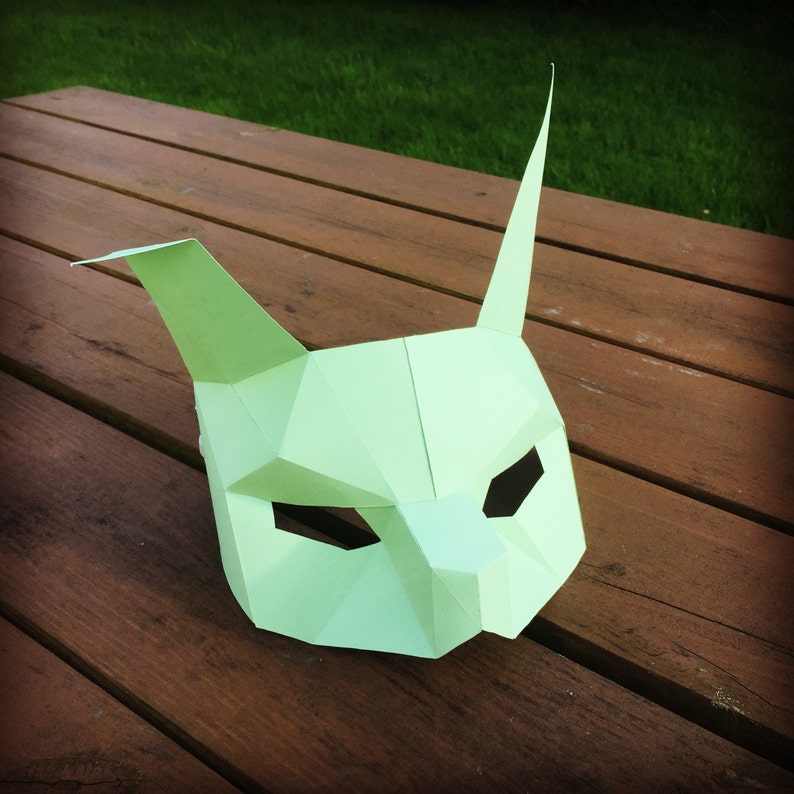 May include: A light green paper mask shaped like an animal face with pointy ears. The mask has cut-out eye holes and a small nose.