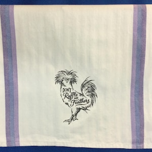 May include: White kitchen towel with purple and blue stripes. The towel has an embroidered image of a rooster with the text "Don't ruffle my feathers".