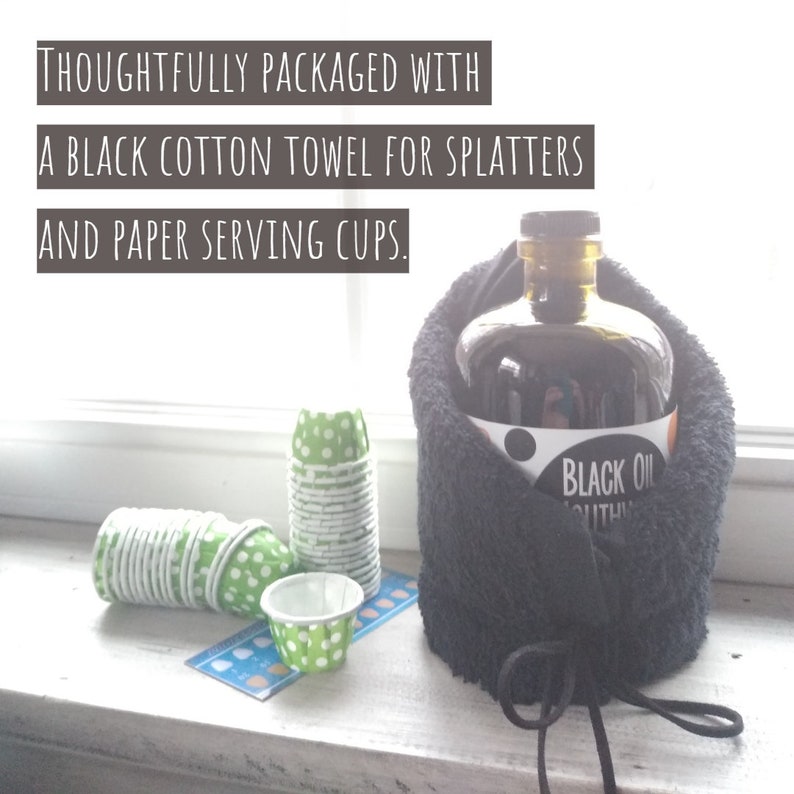 May include: A black cotton towel wrapped around a glass bottle of black oil with a white label that says "BLACK OIL". The bottle is sitting on a white surface next to a stack of green and white paper cups.