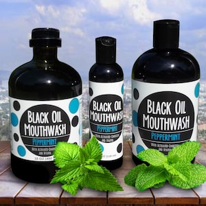 May include: Three bottles of black oil mouthwash with peppermint flavor. The bottles are labeled with the product name and ingredients. The bottles are sitting on a wooden surface with fresh mint leaves.
