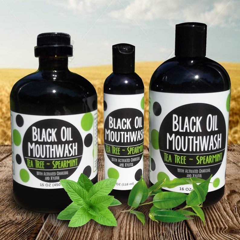 May include: Three bottles of black oil mouthwash with tea tree and spearmint. The bottles are labeled with the product name and ingredients. The bottles are on a wooden surface with green leaves.