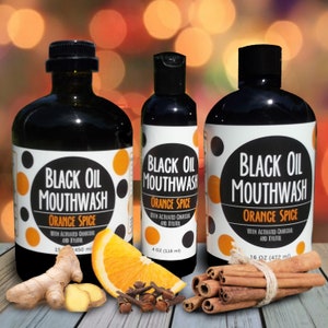 May include: Three bottles of black oil mouthwash with orange spice flavor. The bottles are labeled with the product name and ingredients. The bottles are arranged from smallest to largest. The bottles are sitting on a wooden surface with orange slices, ginger, cinnamon sticks, and cloves.