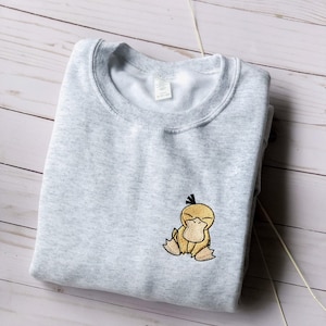 May include: A gray sweatshirt with a yellow embroidered duck on the front. The duck has a black beak and a black eye.