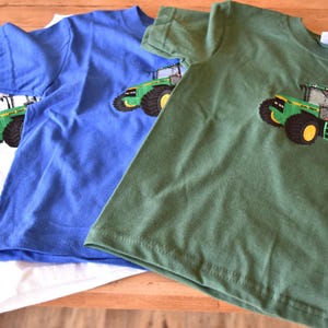 May include: Three short-sleeved t-shirts in white, blue, and green. Each shirt features an embroidered tractor design in green, black, and yellow. The shirts are made of a soft fabric and are suitable for children.