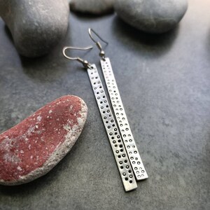 Peut inclure: Une paire de boucles d'oreilles en argent avec un motif texturé. Les boucles d'oreilles sont longues et fines, avec une fermeture simple à crochet.