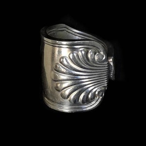 Może przedstawiać: Srebrny pierścionek wykonany z przerobionej łyżki z ozdobnym wzorem muszli.