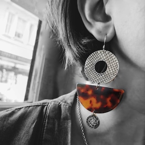 Könnte beinhalten: Ein Paar geometrische Ohrringe mit einem Schildpatt-Design. Die Ohrringe sind aus Metall und haben eine silberne Oberfläche. Die Ohrringe hängen an einem Ohr einer Person.