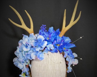 May include: A blue and white floral crown with antlers, perfect for a whimsical or woodland themed event.