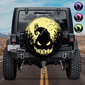 May include: A black spare tyre cover for a vehicle featuring a graphic of a large, glowing yellow moon with a silhouette of a character sitting on a hill, a spooky house, and a large, menacing face with sharp teeth and glowing yellow eyes.