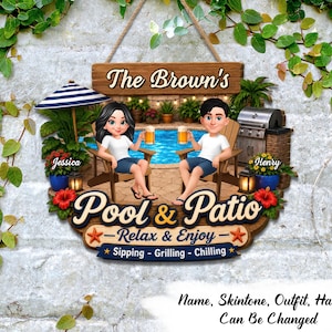 May include: A decorative wooden sign featuring a cartoon illustration of two people sitting by a pool with the text The Brown's, Pool & Patio, Relax & Enjoy, Sipping - Grilling - Chilling, Jessica, and Henry. The sign includes a grill and plants.