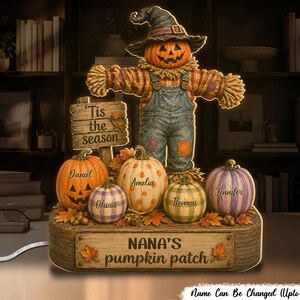 May include: A light-up tabletop decoration featuring a scarecrow with a pumpkin head wearing a hat, standing behind five pumpkins. The pumpkins are personalized with the names Daniel, Olivia, Amelia, Thomas, and Jennifer. A sign reads 'Tis the season' and 'NANA'S pumpkin patch'.