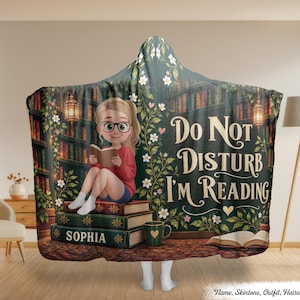 Könnte beinhalten: Eine Kapuzendecke mit einer Zeichentrickfigur mit Brille, die auf einem Bücherstapel sitzt und liest. Das Design zeigt einen Bibliotheks-Hintergrund, Blumenranken und den Text "Do Not Disturb I'm Reading" mit dem Namen "Sophia".