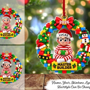 May include: A circular Christmas ornament featuring a wreath made of colorful building blocks, a red bow, and the year 2026. A cartoon character in red and white striped pajamas sits in the center, holding a green block. Text reads LUCAS and MASTER BUILDER.