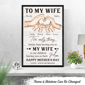 Puede incluir: Un cartel enmarcado con el texto "TO MY WIFE" y un corazón hecho con manos. El cartel incluye nombres y el mensaje "HAPPY MOTHER'S DAY". El fondo es un patrón de vetas de madera clara.
