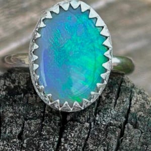 May include: A silver ring with a blue and green opal gemstone set in a jagged, silver bezel.