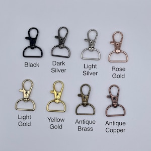 May include: Eight metal lobster claw clasps with D-rings in various finishes: black, dark silver, light silver, rose gold, light gold, yellow gold, antique brass, and antique copper. Each clasp is labeled with its corresponding color name below it.