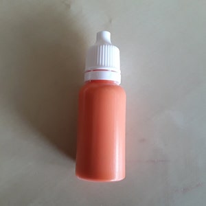 May include: A small, orange plastic bottle with a white dropper top. The bottle is about 7.5 cm tall.