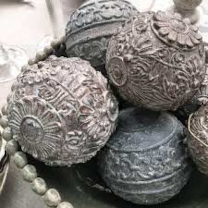 Puede incluir: Cinco esferas decorativas con intrincados dise&ntilde;os en relieve en tonos grises y marrones. Las esferas est&aacute;n dispuestas en un cuenco.