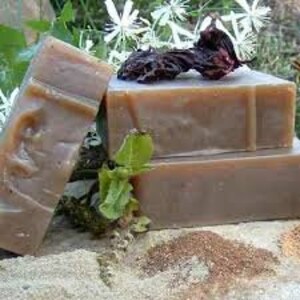 Puede incluir: Tres barras de jab&oacute;n hechas a mano, apiladas una encima de la otra. El jab&oacute;n es de color marr&oacute;n claro y tiene un aspecto natural y terroso. El jab&oacute;n est&aacute; rodeado de flores y hojas secas.