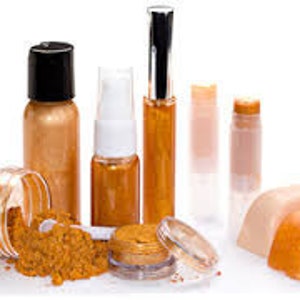 Puede incluir: Un conjunto de productos cosméticos dorados que incluye un tarro de polvo, una botella de líquido, una botella de spray, un tubo de brillo de labios, un bálsamo labial en barra y dos barras sólidas de maquillaje.