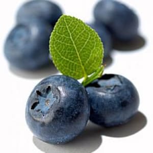 May include: Close-up of several blueberries with a single green leaf on top. The blueberries are a deep blue colour and have a slightly shiny surface.