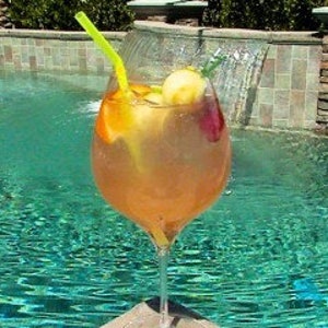 May include: A glass of pink sangria with fruit and a green straw, sitting by a swimming pool.
