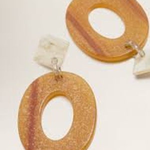 May include: A pair of oval-shaped wooden earrings with a white and brown marbled design. The earrings have a dangling charm with a white and brown marbled design.