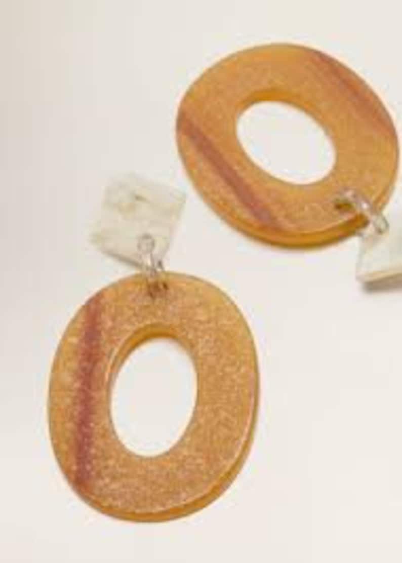 May include: A pair of oval-shaped wooden earrings with a white and brown marbled design. The earrings have a dangling charm with a white and brown marbled design.