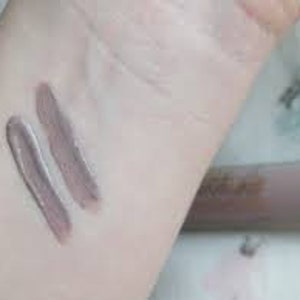 Puede incluir: Dos muestras de una sombra de ojos crema marr&oacute;n claro en la mu&ntilde;eca de una persona. La sombra de ojos est&aacute; en un tubo con una tapa dorada.