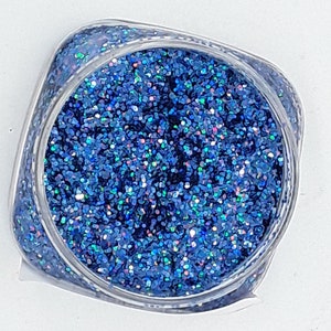 May include: A small clear jar filled with blue glitter. The glitter has a holographic finish, with iridescent blue, green, and purple hues.