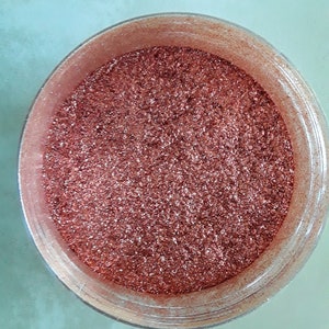 May include: A close-up view of a small, clear container filled with fine, copper-coloured glitter.